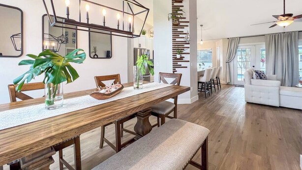 A modern dining area with a wooden table, benches, and a geometric pendant light. - Ruby's Retreat, heated pool, private oasis, fenced backyard (Cape Coral)