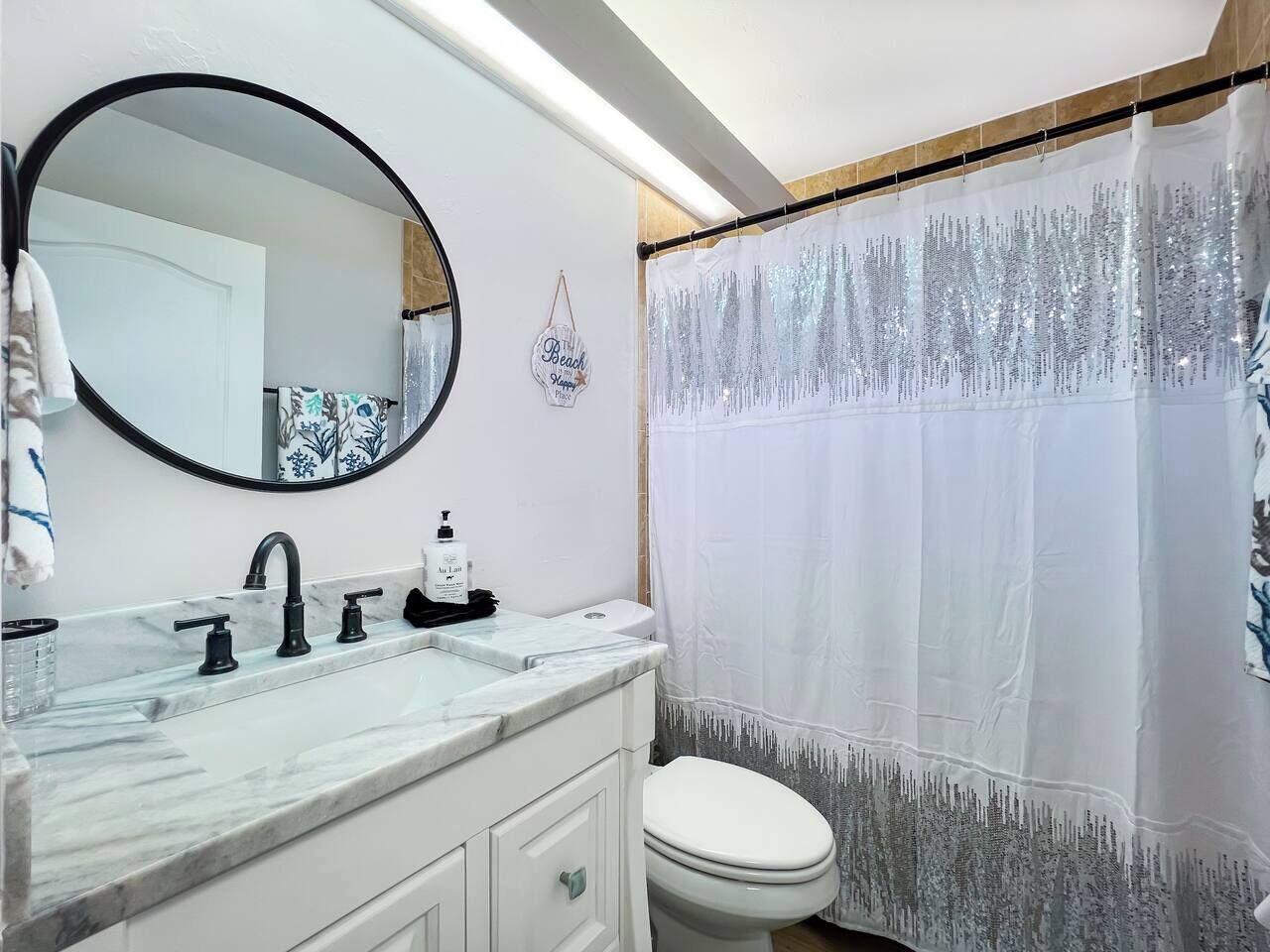 A bathroom with a white sink, black faucets, a mirror, a toilet, and a shower curtain with a silver pattern.