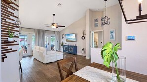 A spacious living area with a white sofa, wooden dining table, and a large plant. - Ruby's Retreat, heated pool, private oasis, fenced backyard (Cape Coral)