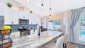 A modern kitchen with white cabinets, a marble island, and pendant lighting. - Ruby's Retreat, heated pool, private oasis, fenced backyard (Cape Coral)