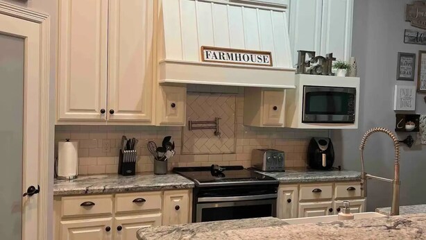 A kitchen with white cabinets, a farmhouse sign, a microwave, a stove, and a pendant light. - Main House Listing 3BD/2BA

 (Edinburg)