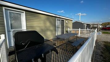 A mobile home with a deck, a barbecue grill, and a table.