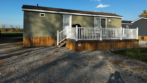 A single-story mobile home with a front porch and a gravel driveway. - Beautiful Cottage (508) in Vineyards of Niagara On The Lake (Niagara-on-the-Lake)