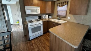 A compact kitchen with a microwave, stove, sink, and wooden cabinets. - Beautiful Cottage (508) in Vineyards of Niagara On The Lake (Niagara-on-the-Lake)