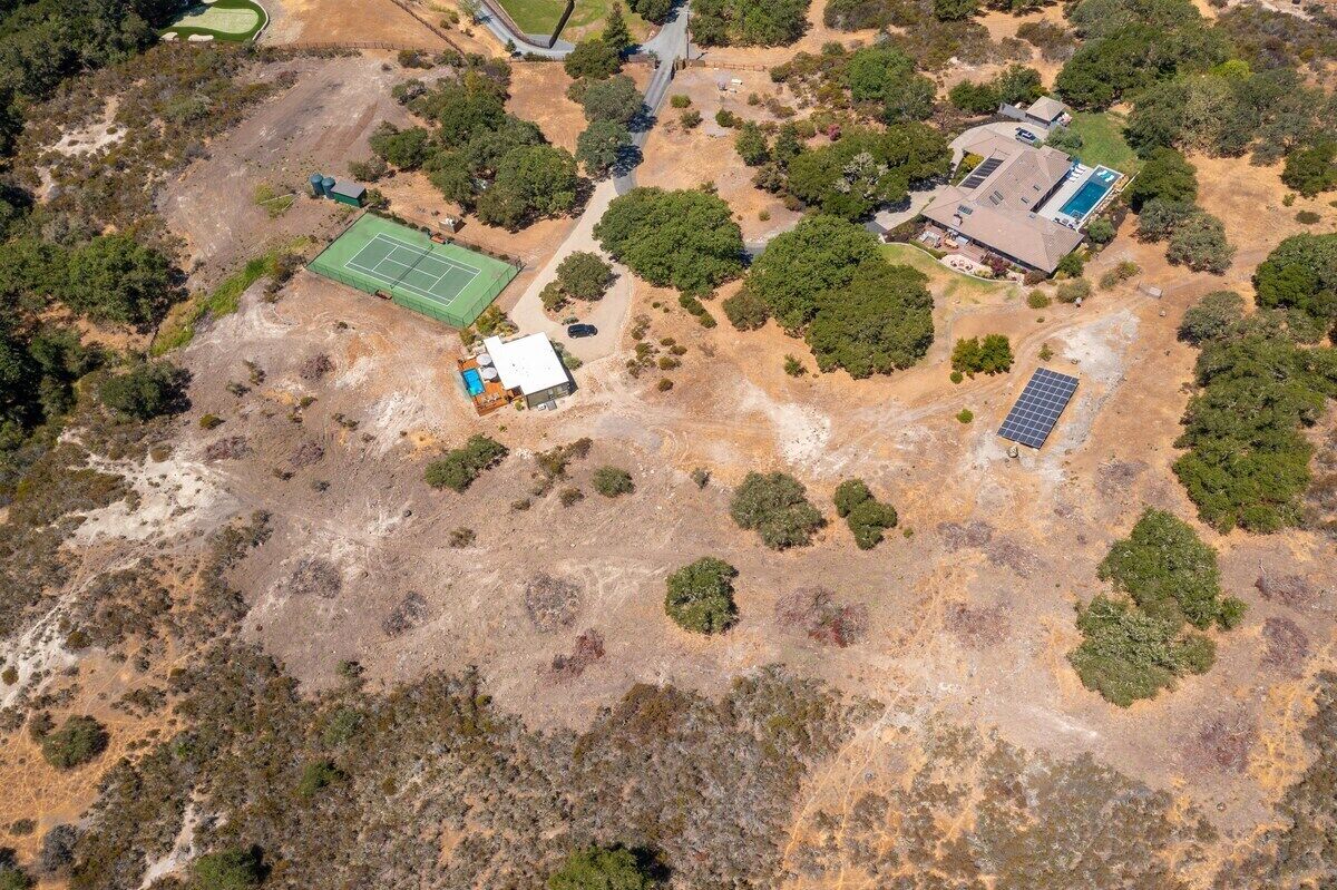 An aerial view of a property with a tennis court, a swimming pool, and solar panels.