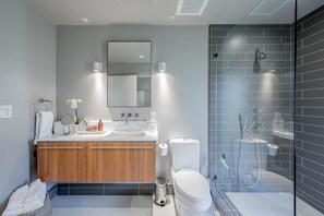 A modern bathroom with a wooden vanity, a large mirror, a toilet, and a glass-enclosed shower area.