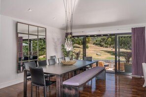 A modern dining area with a large table, chairs, and a bench. A large mirror and hanging light fixture are visible. - Calistoga Wine Ranch (Calistoga)