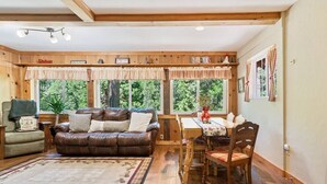 A cozy cabin interior with a leather couch, wooden dining table, and a large window with curtains. - Fire Pit • King Bed Sugar Pine Retreat, Yosemite (Oakhurst)