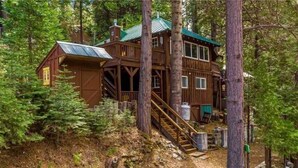 A wooden cabin with a staircase leading to a deck, surrounded by trees. - Fire Pit • King Bed Sugar Pine Retreat, Yosemite (Oakhurst)
