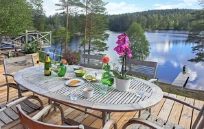 En træterrasse med et rundt spisebord, med udsigt over en sø med skovkant.