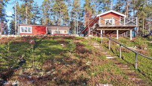 A cabin with a red exterior, a covered porch, and a stone foundation.
