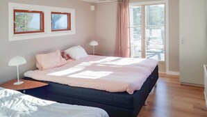 A bedroom with a large bed, two bedside tables, a window with curtains, and a view of a deck.