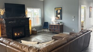 Un vaste salon comprenant un grand canapé d’angle en cuir, une cheminée, un téléviseur à écran plat et deux ventilateurs de plafond.