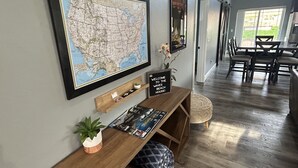Un couloir avec une console en bois, une carte, un panneau d’accueil et une vue sur un coin repas.
