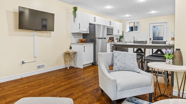 A modern kitchen with white cabinets, stainless steel appliances, and a flat-screen TV mounted on the wall.