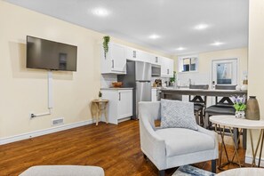 A modern kitchen with white cabinets, stainless steel appliances, and a flat-screen TV mounted on the wall.