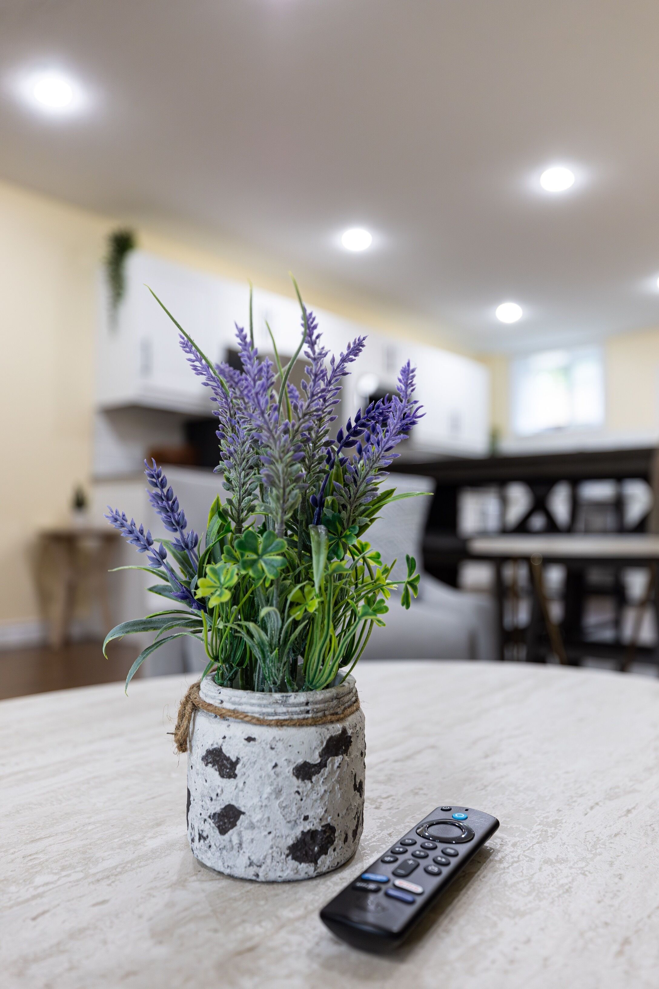 A remote control on a table next to a rustic vase with lavender plants.