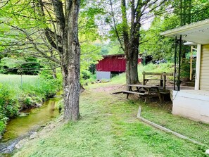 Sit by the serene stream and enjoy the peaceful surroundings near the rustic barn.
