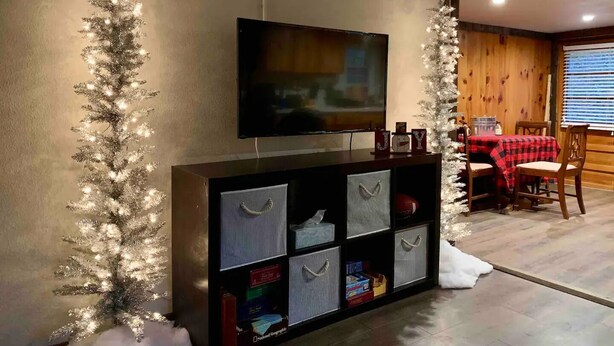 A living room with a TV mounted on the wall, a fireplace, and a dining area with a table and chairs. - Creekside Cabin skiing/hiking & Appalachian Trail. (Green Mountain)