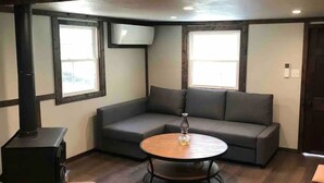 A cozy living room with a sectional sofa, a round wooden coffee table, and a black wood-burning stove. - Creekside Cabin skiing/hiking & Appalachian Trail. (Green Mountain)