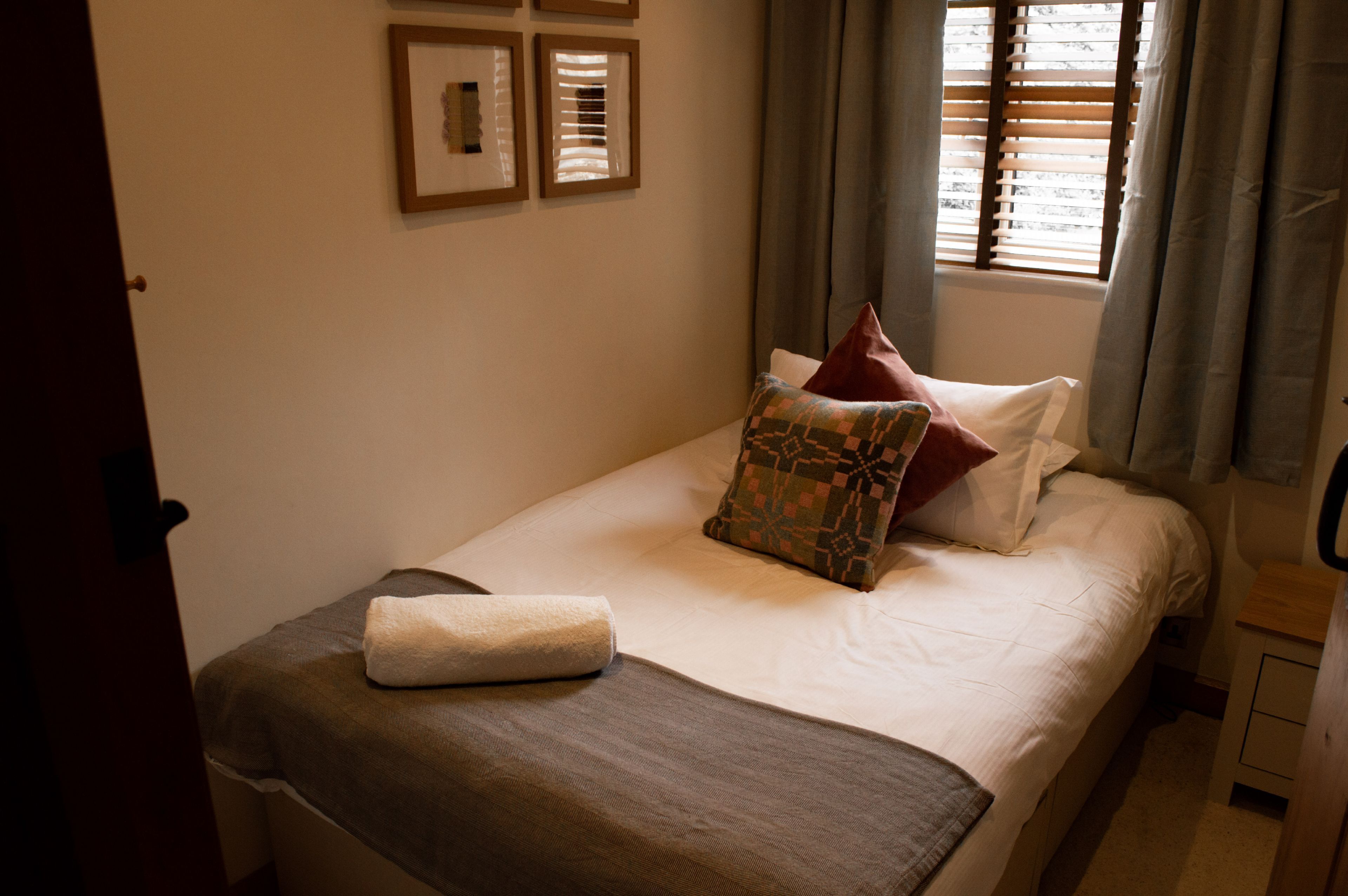 A neatly made bed with a brown blanket, a patterned pillow, and a rolled towel.