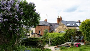 Un jardin résidentiel avec une maison en briques, une pelouse et un petit espace extérieur aménagé pour s’asseoir.