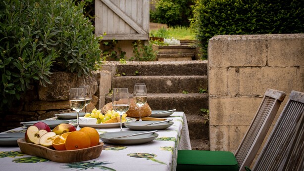 Une table dressée à l’extérieur, avec des fruits, du pain et des verres à vin.