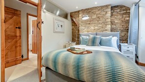 Une chambre avec un mur en pierre, un lit avec une literie bleue, une porte en bois et une table de chevet avec une lampe.