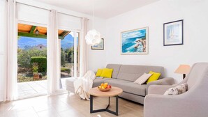 A modern living room with a grey sofa, yellow cushions, a round wooden coffee table with fruit, and a view of a coastal landscape through large glass doors. - Holiday house Sunshine in center of Jelsa (Jelsa)