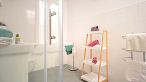 A modern bathroom with a glass shower enclosure, a white sink, and a wooden shelf unit holding towels. - Holiday house Sunshine in center of Jelsa (Jelsa)