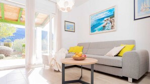 A modern living room with a grey sofa, a round wooden coffee table, and a bowl of fruit. There are two framed pictures on the wall, one depicting a beach scene and another with a blue sky. - Holiday house Sunshine in center of Jelsa (Jelsa)