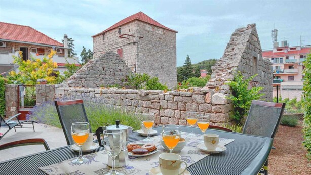 A table set outdoors with breakfast items, a stone wall, and a stone tower in the background. - Holiday house Sunshine in center of Jelsa (Jelsa)