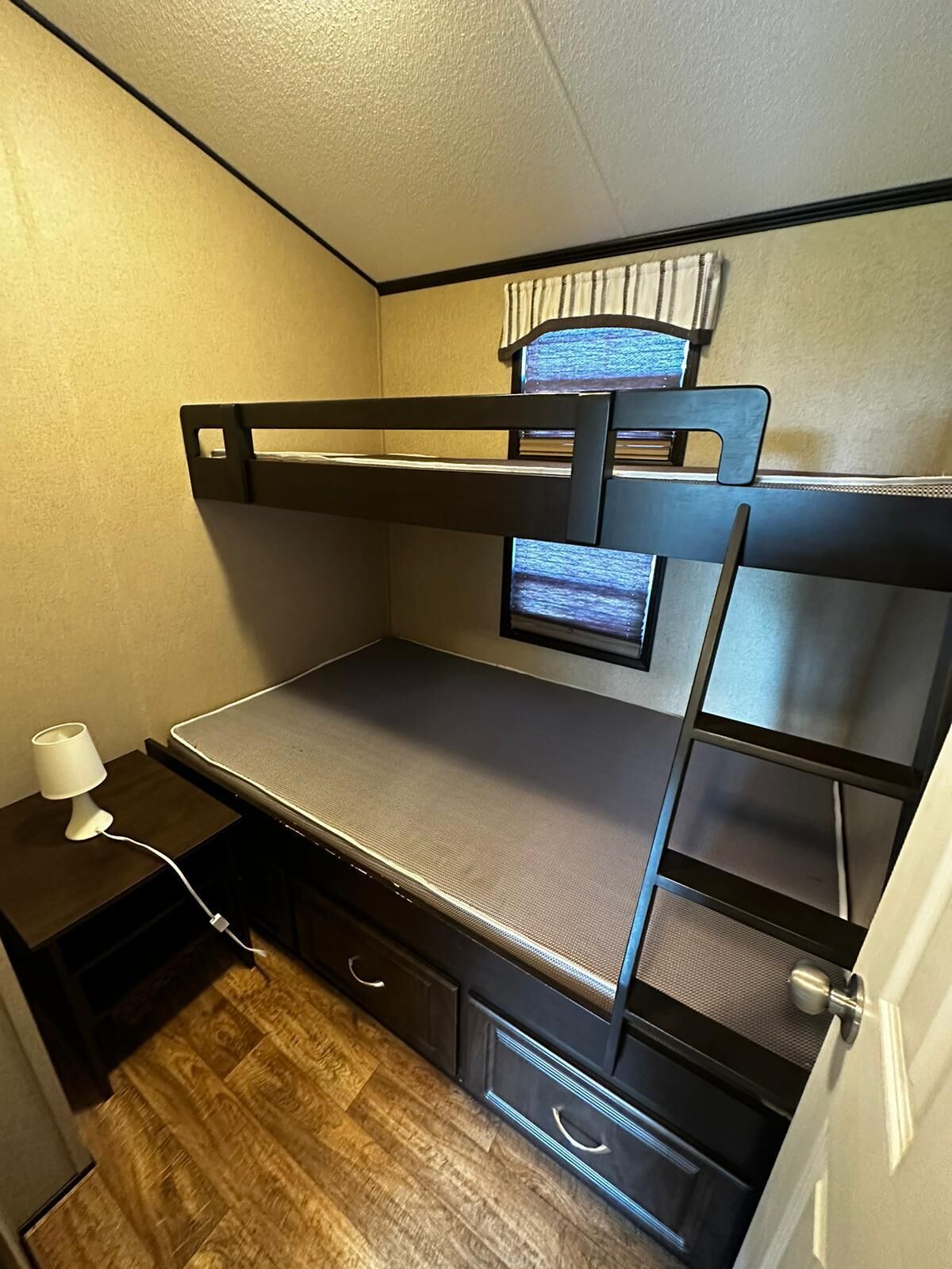 Un lit superposé avec un téléviseur sur le lit du haut, une table de chevet avec une lampe et un plancher en bois.