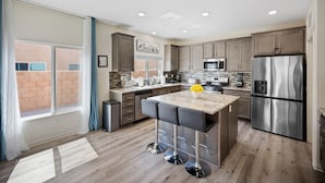 A modern kitchen with a central island, stainless steel appliances, and a view to the outside. - Family Paradise Saltwater Pool & Spa Game Room Fire Pit  EV Charger  Poker Table (Desert Hot Springs)