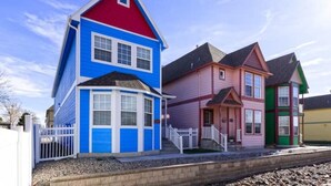 Eine Reihe von farbenfrohen Häusern mit unterschiedlichen Baustilen, darunter ein blaues Haus mit rotem Dach und ein rosa Haus mit grüner Tür.