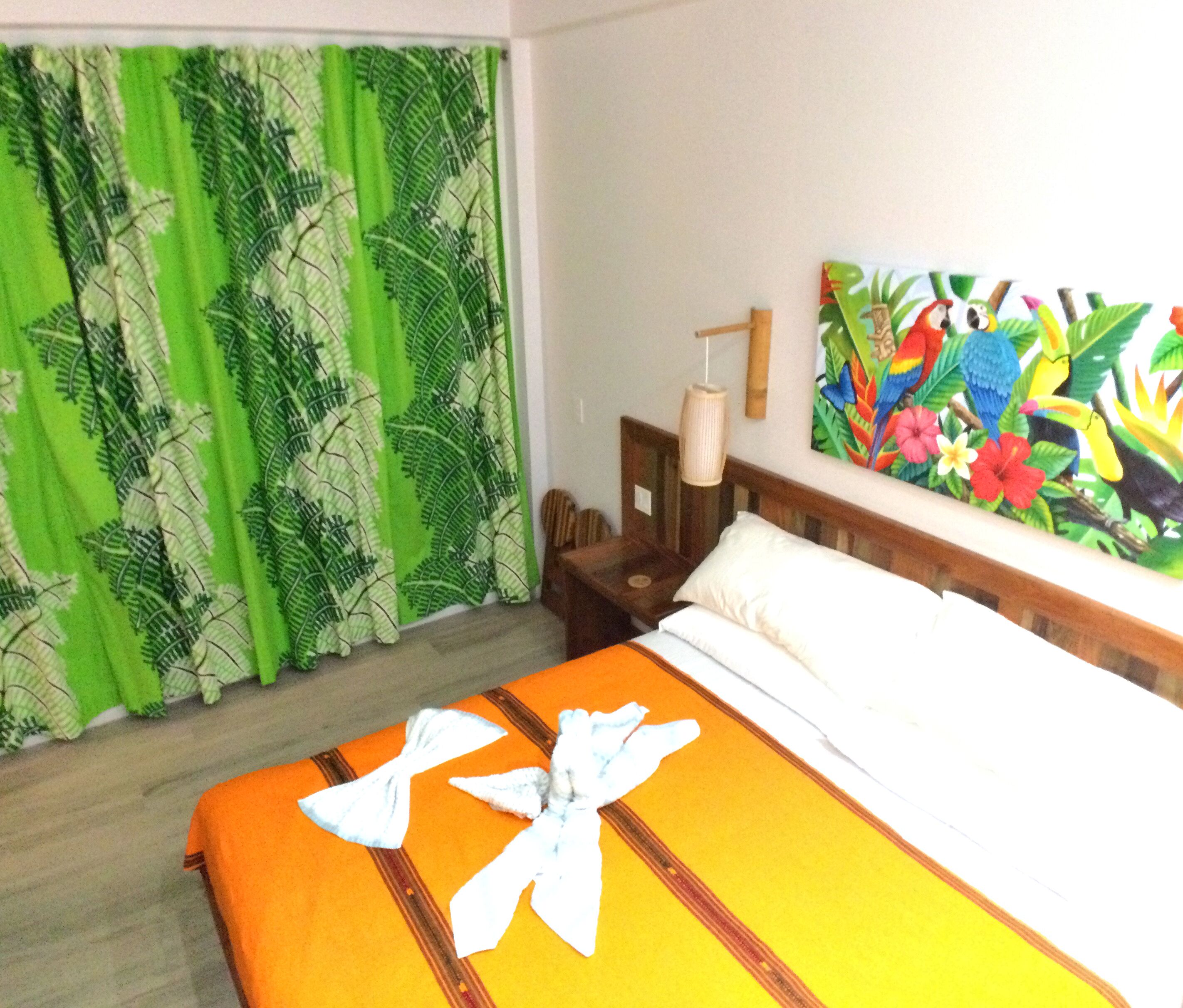 A hotel room with a bed, green curtains, a painting, and a nightstand.