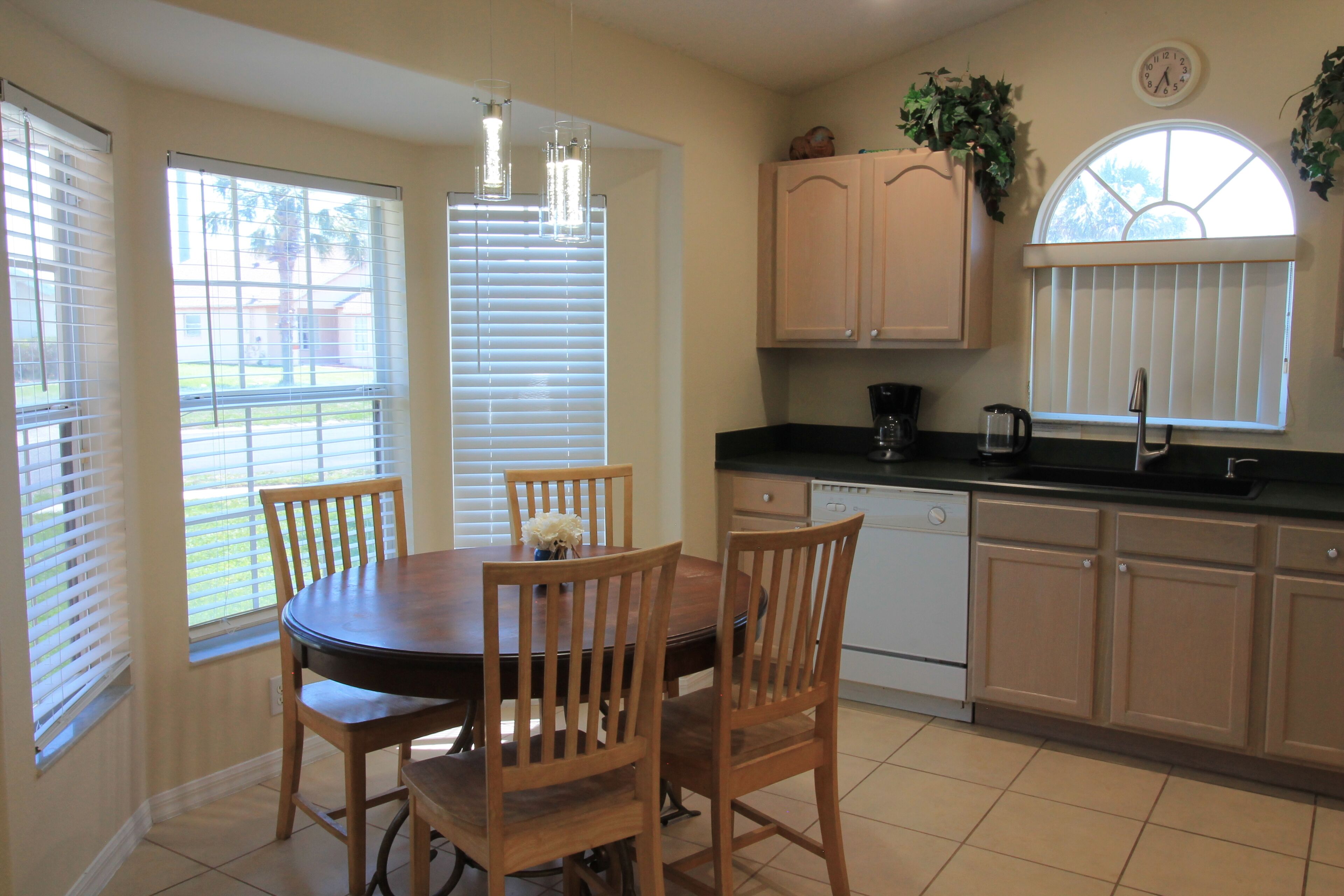 A dining area with a wooden table and chairs, a kitchen with cabinets and appliances, and a window with blinds.