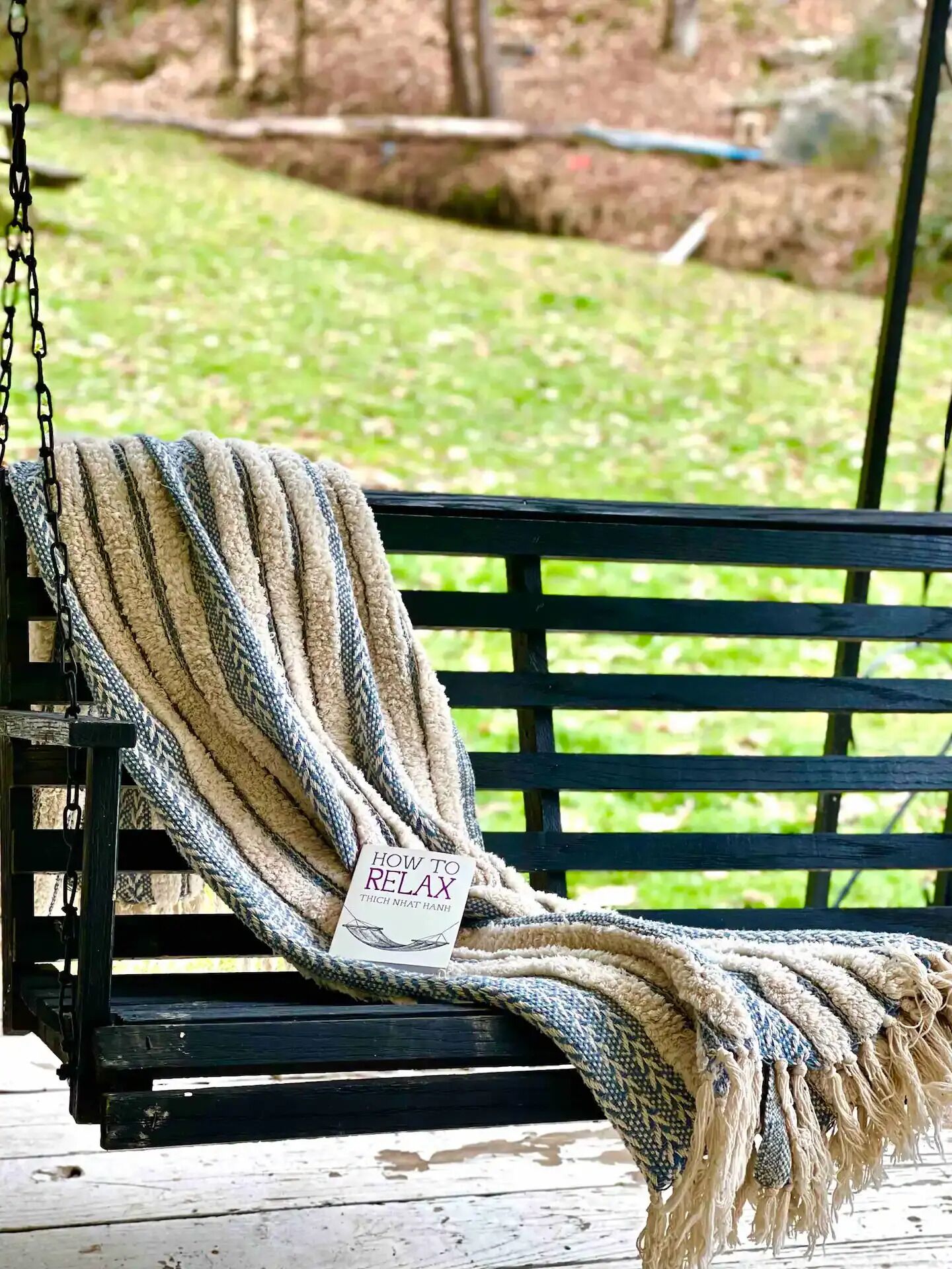 A black wooden bench with a beige and blue striped throw blanket draped over it.