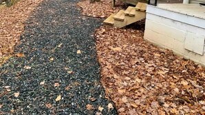 Ein Kiesweg führt zu einem Gebäude mit einer Veranda, umgeben von Bäumen und einem roten Schuppen.