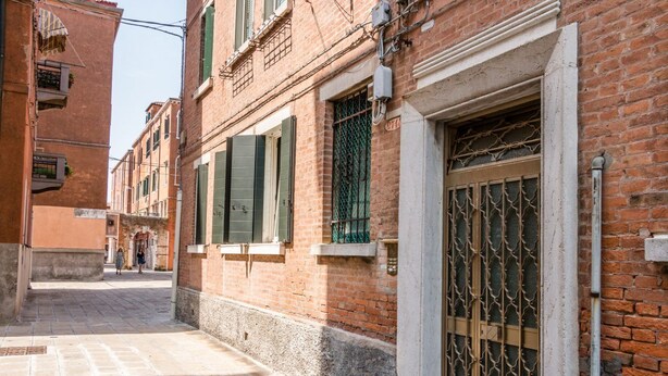 Una stretta via fiancheggiata da edifici tradizionali, un cancello in metallo e un cielo sereno.