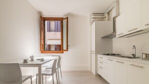 Una cucina compatta con mobili bianchi, un tavolo da pranzo con sedie e una finestra con persiane aperte.