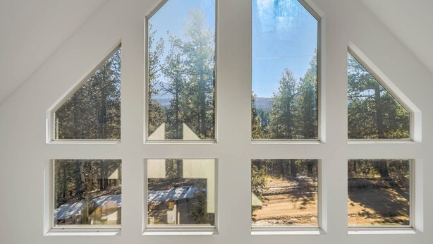 Habitació amb sostre inclinat i diverses finestres que donen vista a una zona boscosa.