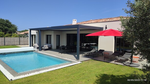 A modern outdoor pool area with a covered patio, lounge chairs, and a red umbrella. - Villa à 800 Mètres Cœur du Village Accessible à Pied, Secteur Sécurisé et Calme (Saint-Rémy-de-Provence)