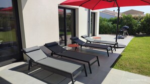 A modern outdoor patio with sun loungers and a red umbrella, featuring a glass wall and a well-maintained lawn. - Villa à 800 Mètres Cœur du Village Accessible à Pied, Secteur Sécurisé et Calme (Saint-Rémy-de-Provence)