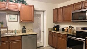 Una cocina con armarios de madera, lavavajillas de acero inoxidable, microondas y horno.