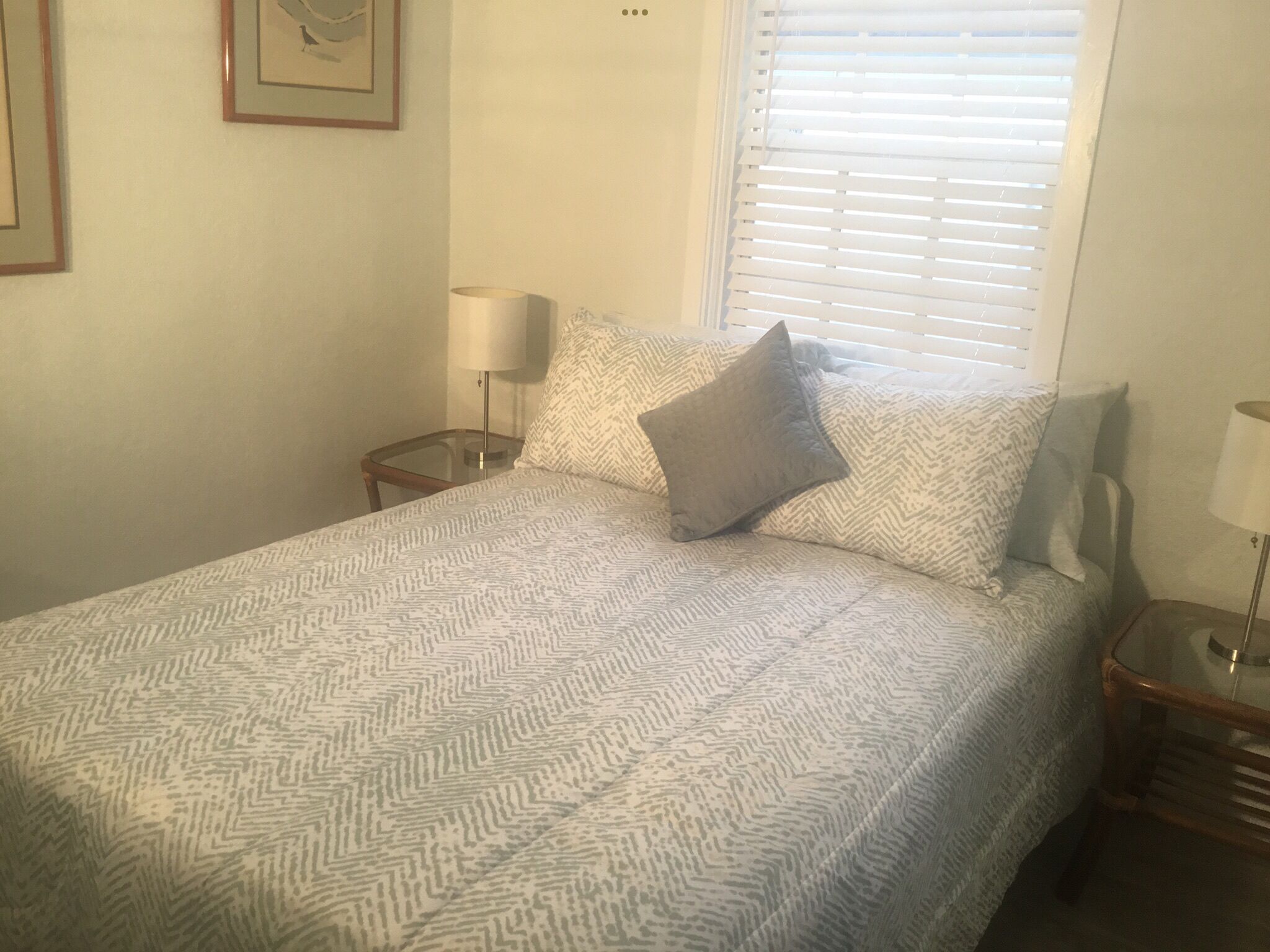 A neatly made bed with patterned bedding, a bedside lamp, and a window with blinds.