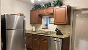 Una cocina compacta con electrodomésticos de acero inoxidable, armarios de madera y encimera de granito.