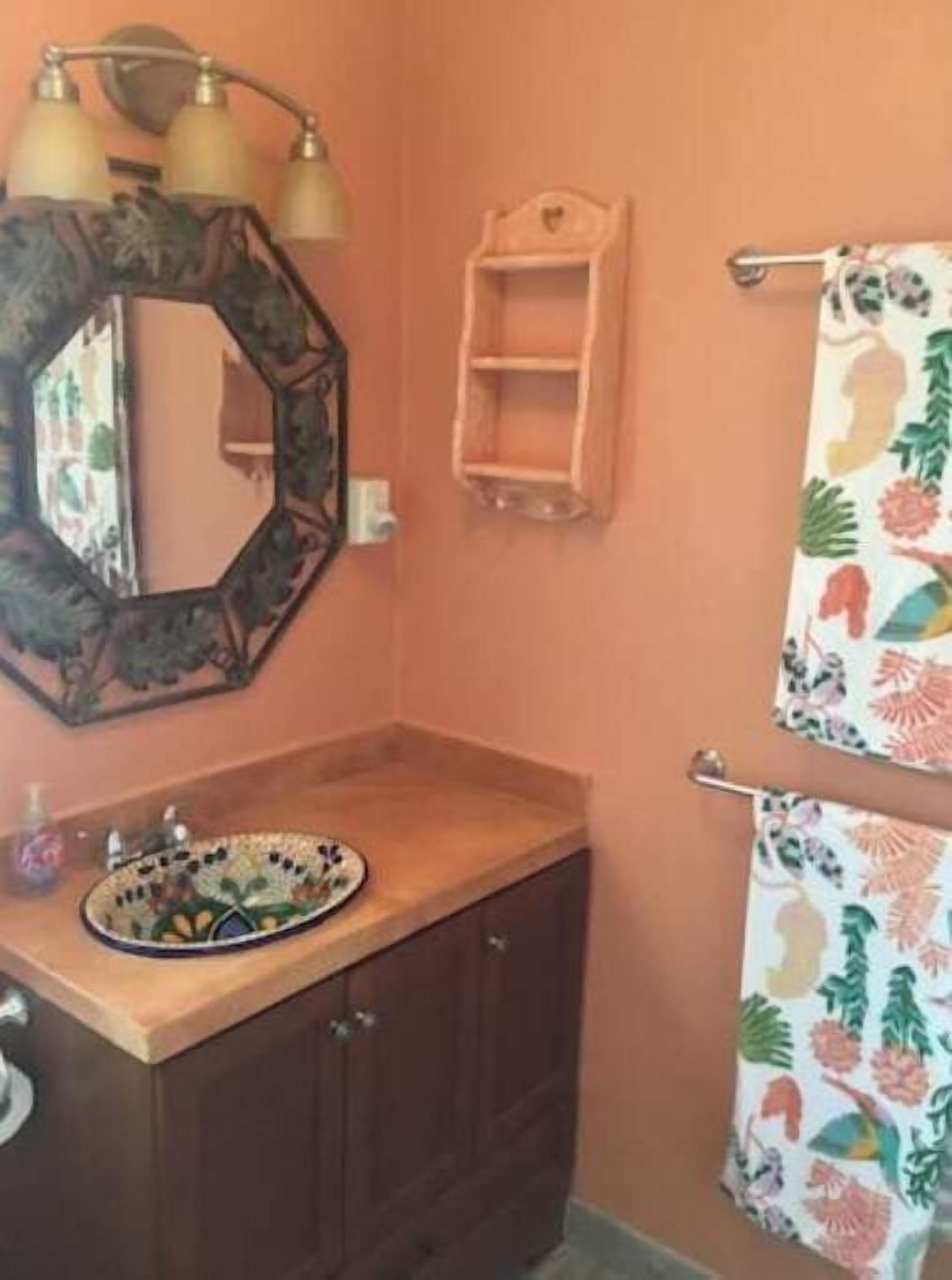 A bathroom with a wooden vanity, a mirror with a decorative frame, a sink with a patterned basin, a towel rack with a floral towel, and a small shelf unit.