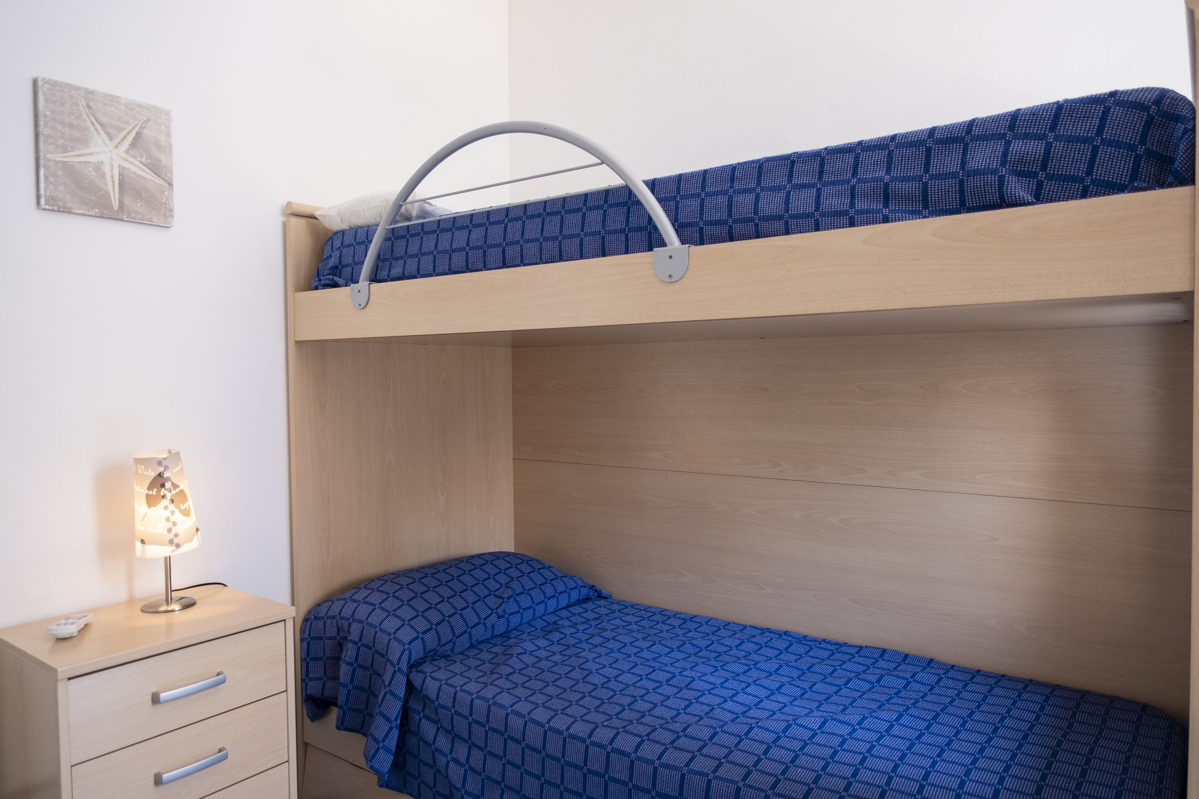 Un lit superposé avec une tête de lit, une table de chevet avec des tiroirs et une lampe fixée au mur.