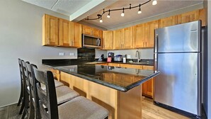 Une cuisine moderne avec des meubles en bois, un réfrigérateur en acier inoxydable, un four à micro-ondes encastré et un coin bar avec des sièges.